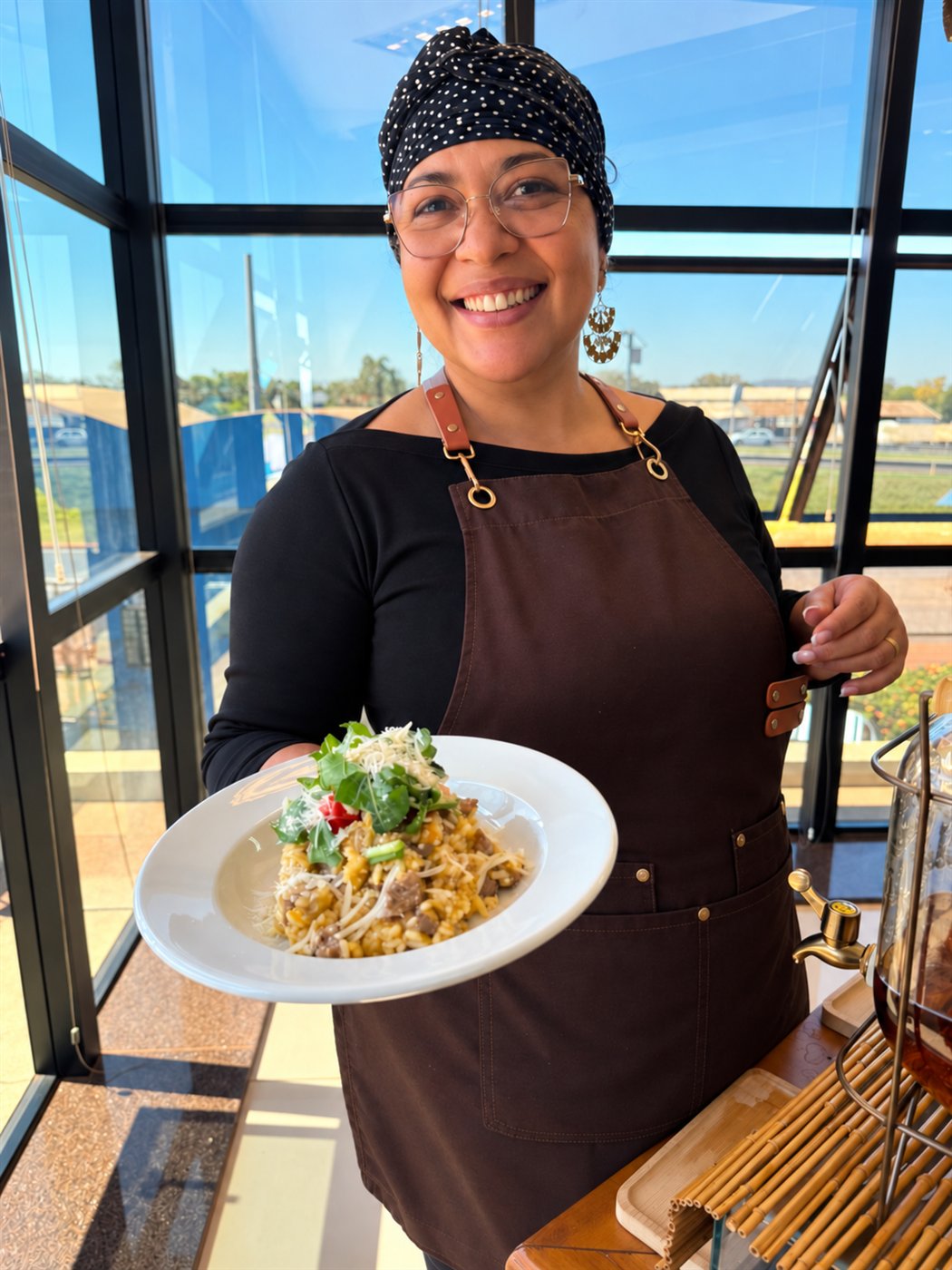 Carla Camilo na cozinha, sorrindo, servindo um prato de risoto
