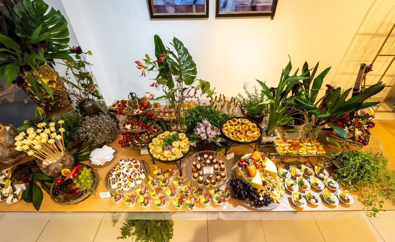 A mesa inteira vista do alto, com canapés, tortinhas, queijos, frutas e folhagens